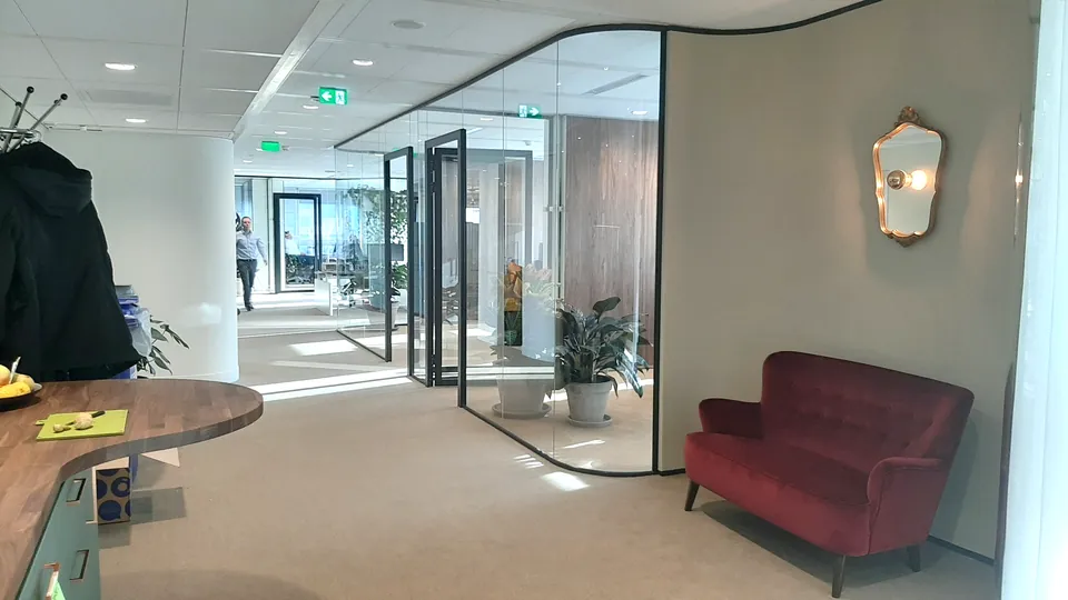 Glazen overlegruimtes en een rode bank in het kantoor van Schroders Real Estate
